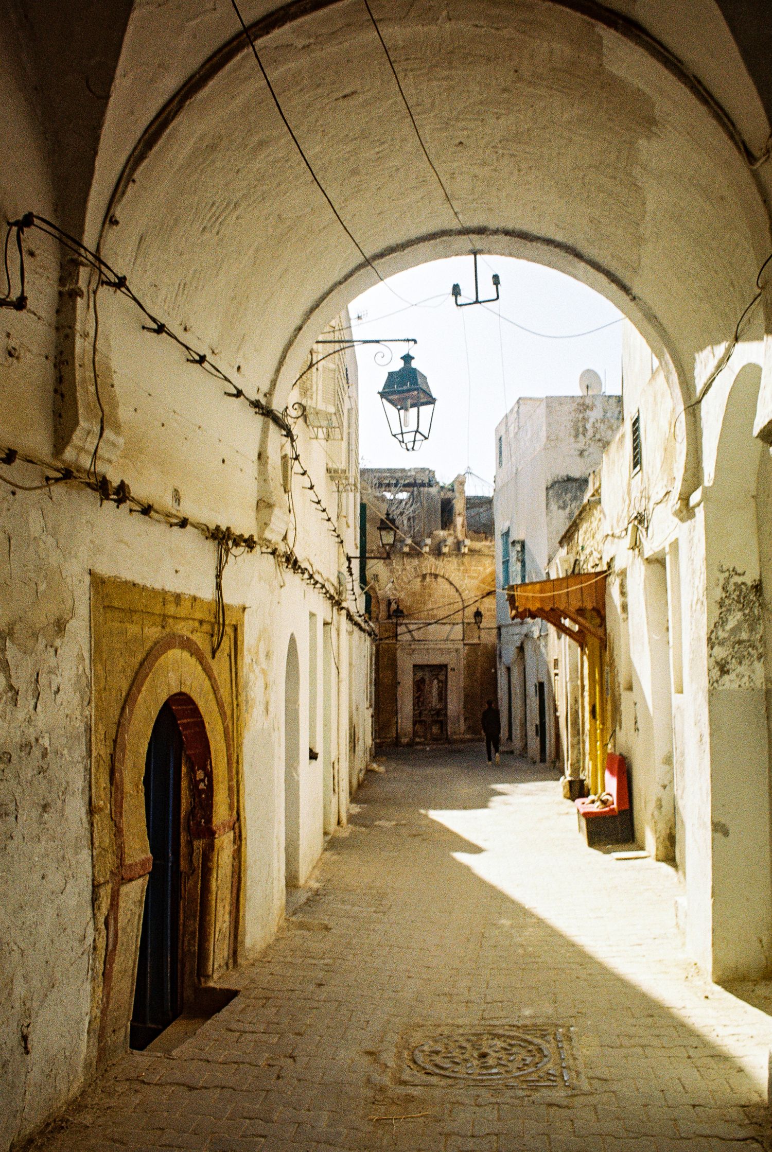 Ancient arched alleyway in a traditional Moroccan medina with white walls, ornate doorways and hanging lanterns.