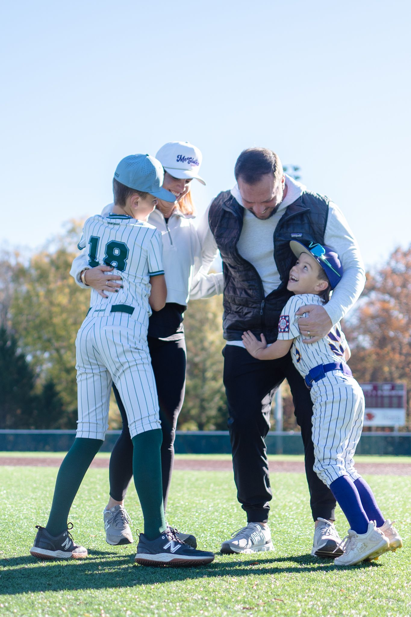 Youth baseball players and coach interact on sunny field during practice while wearing pinstriped uniforms.