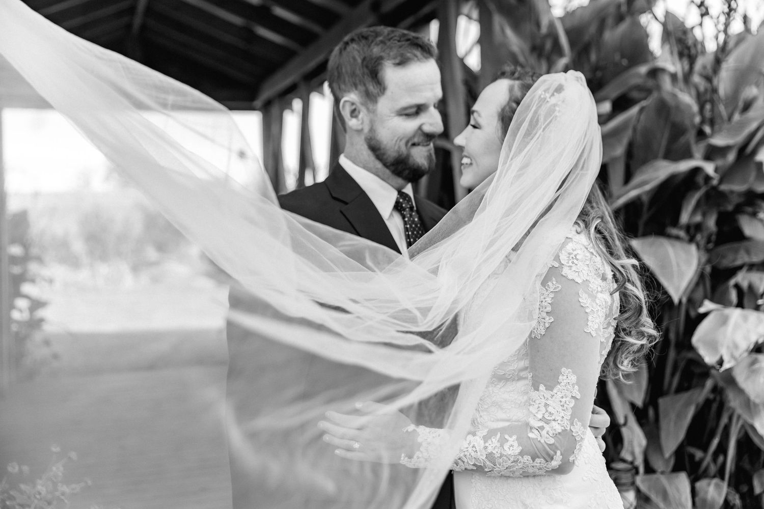 Black and white wedding portrait with flowing veil creating dramatic effect.