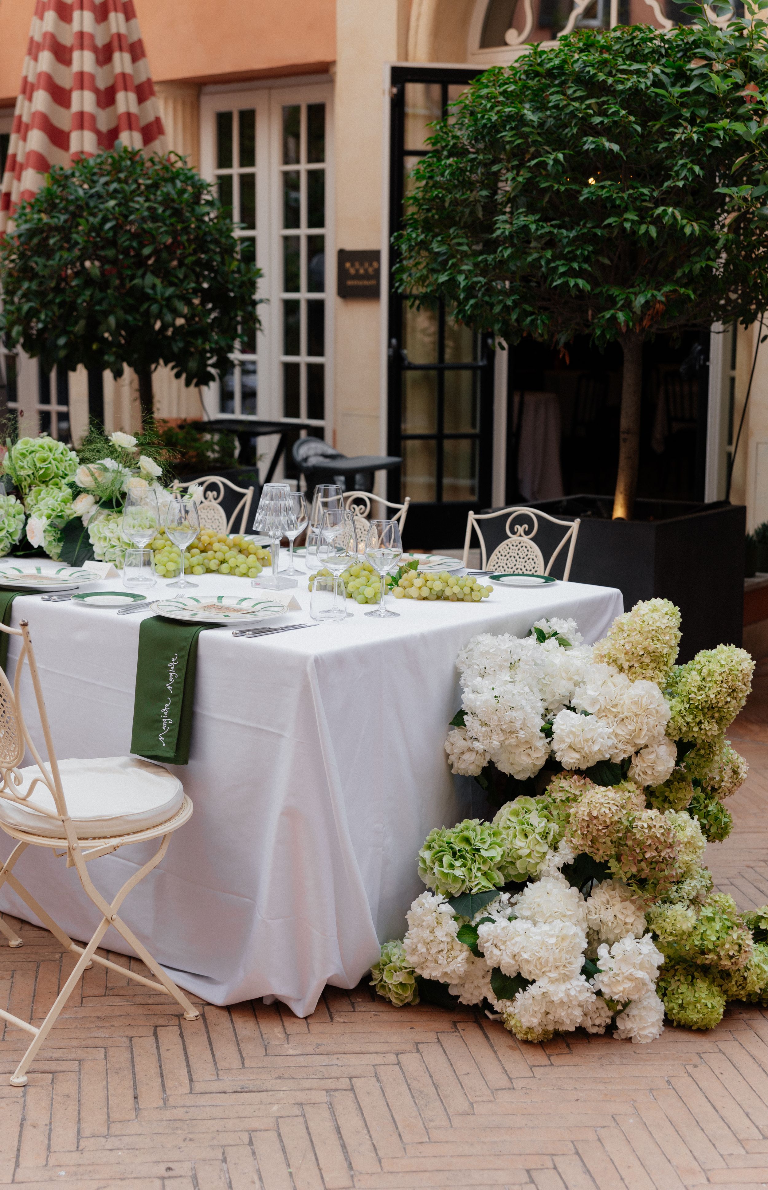 Elegant outdoor wedding reception setup with white tablecloths and hydrangea floral arrangements on a brick patio.