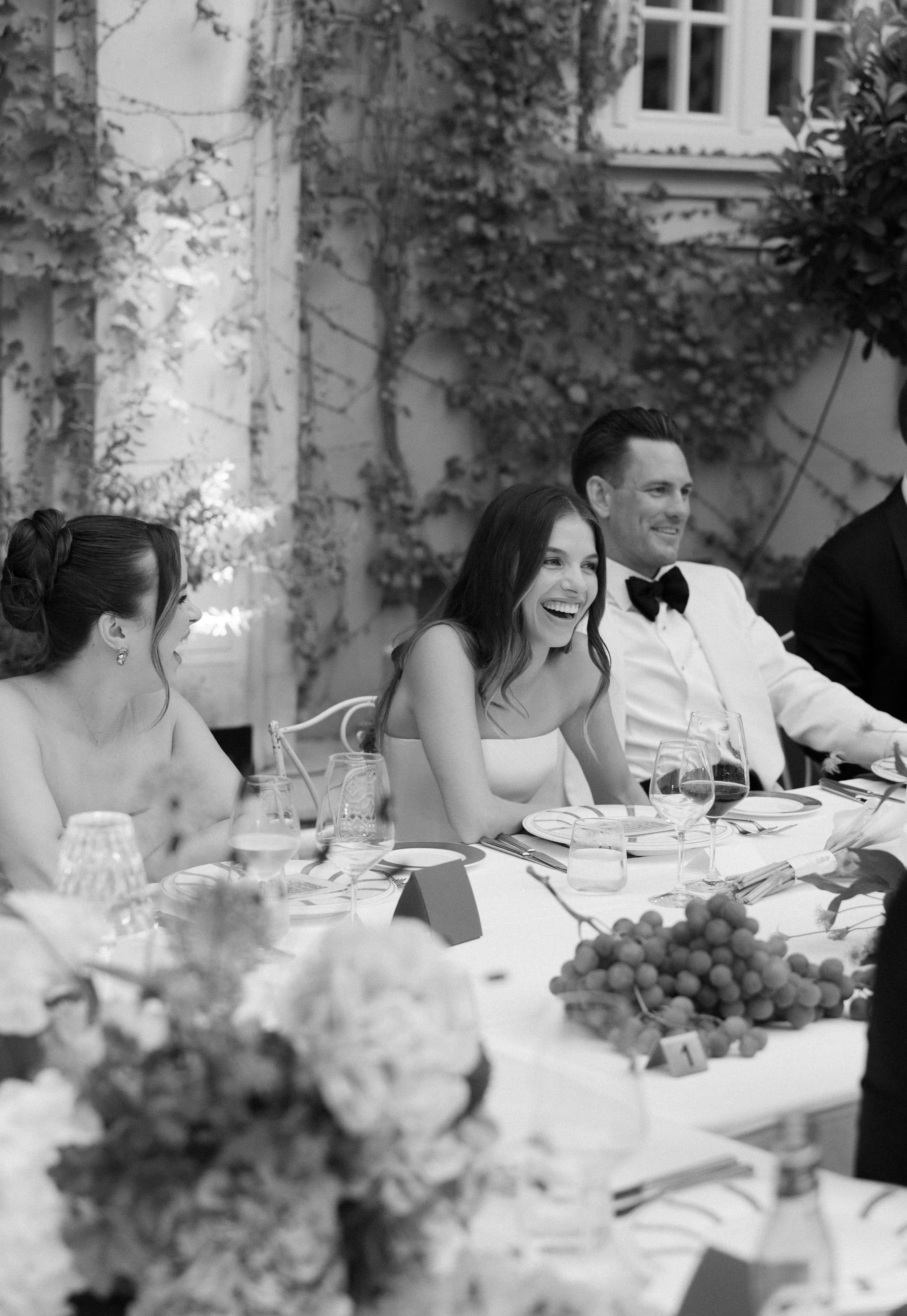 Guests enjoying an elegant outdoor dinner party with wine glasses and grapes on a beautifully set table.