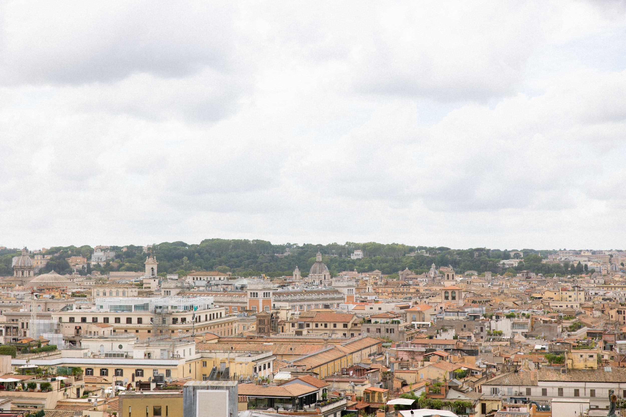 Panoramic aerial view of Rome's historic cityscape with ancient architecture and terracotta rooftops under cloudy skies.