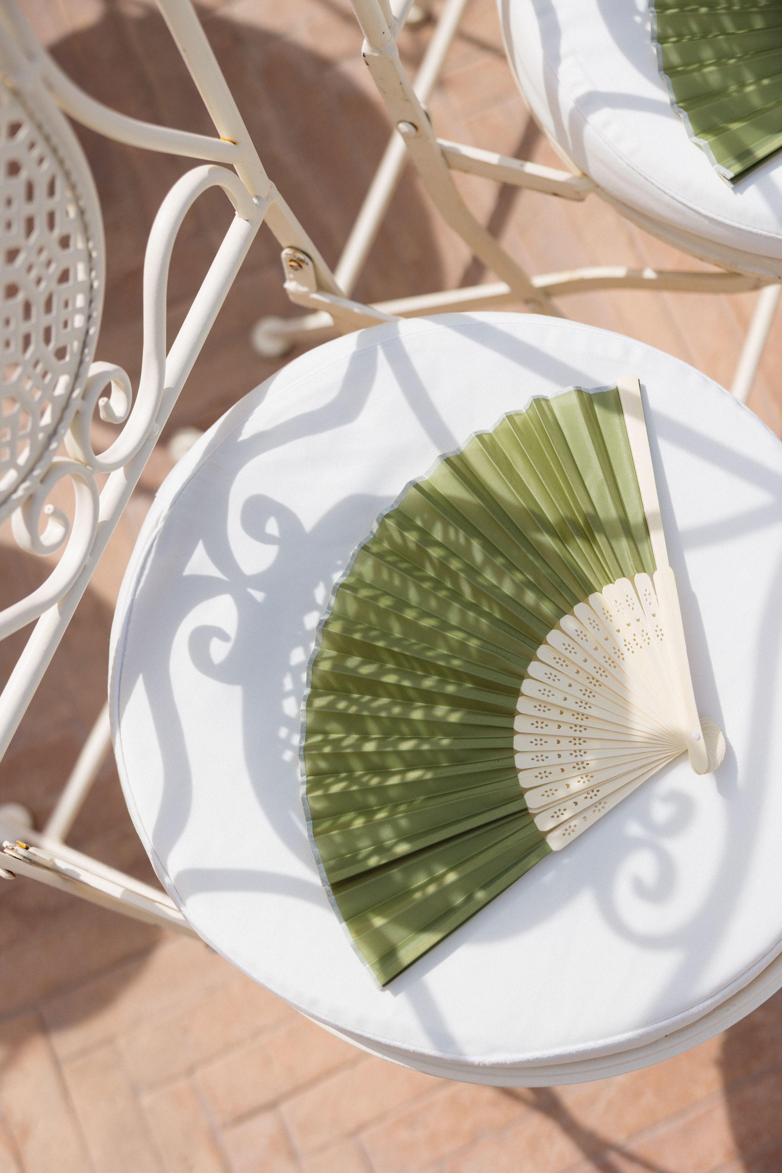 Decorative green and white folding paper fans arranged on white plates against a terracotta tile background.