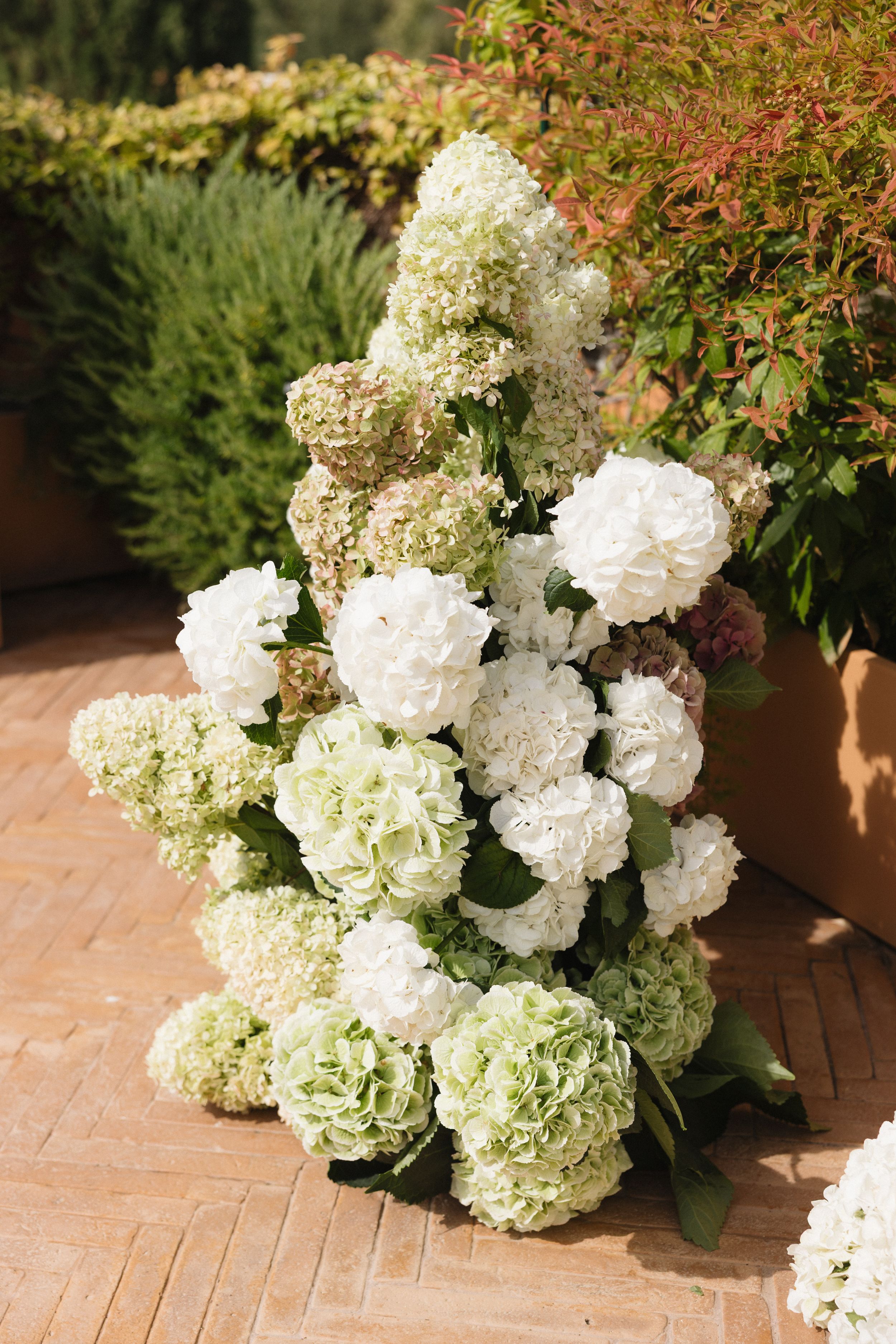 White and cream hydrangea flower arrangements displayed on a terracotta patio create an elegant garden setting.