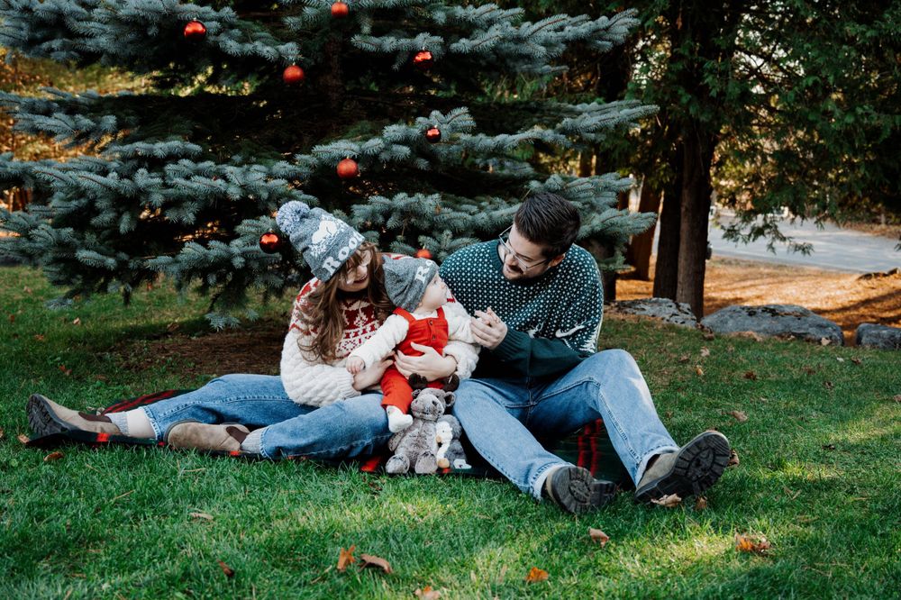 A family relaxes on grass near blue spruce trees with a small dog during an autumn afternoon.
