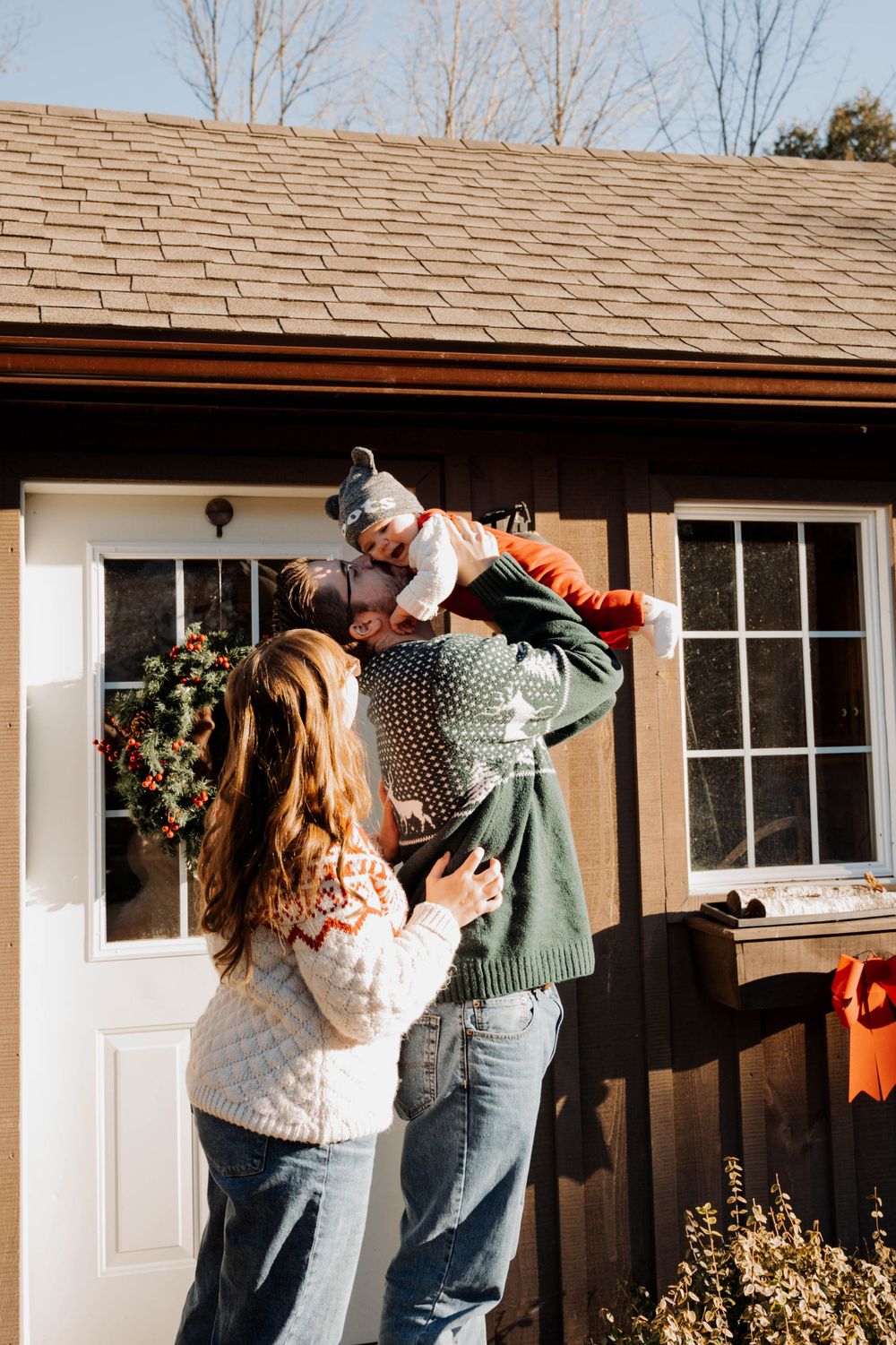 Family enjoying playful moment with small dog outside rustic cabin decorated for holidays.