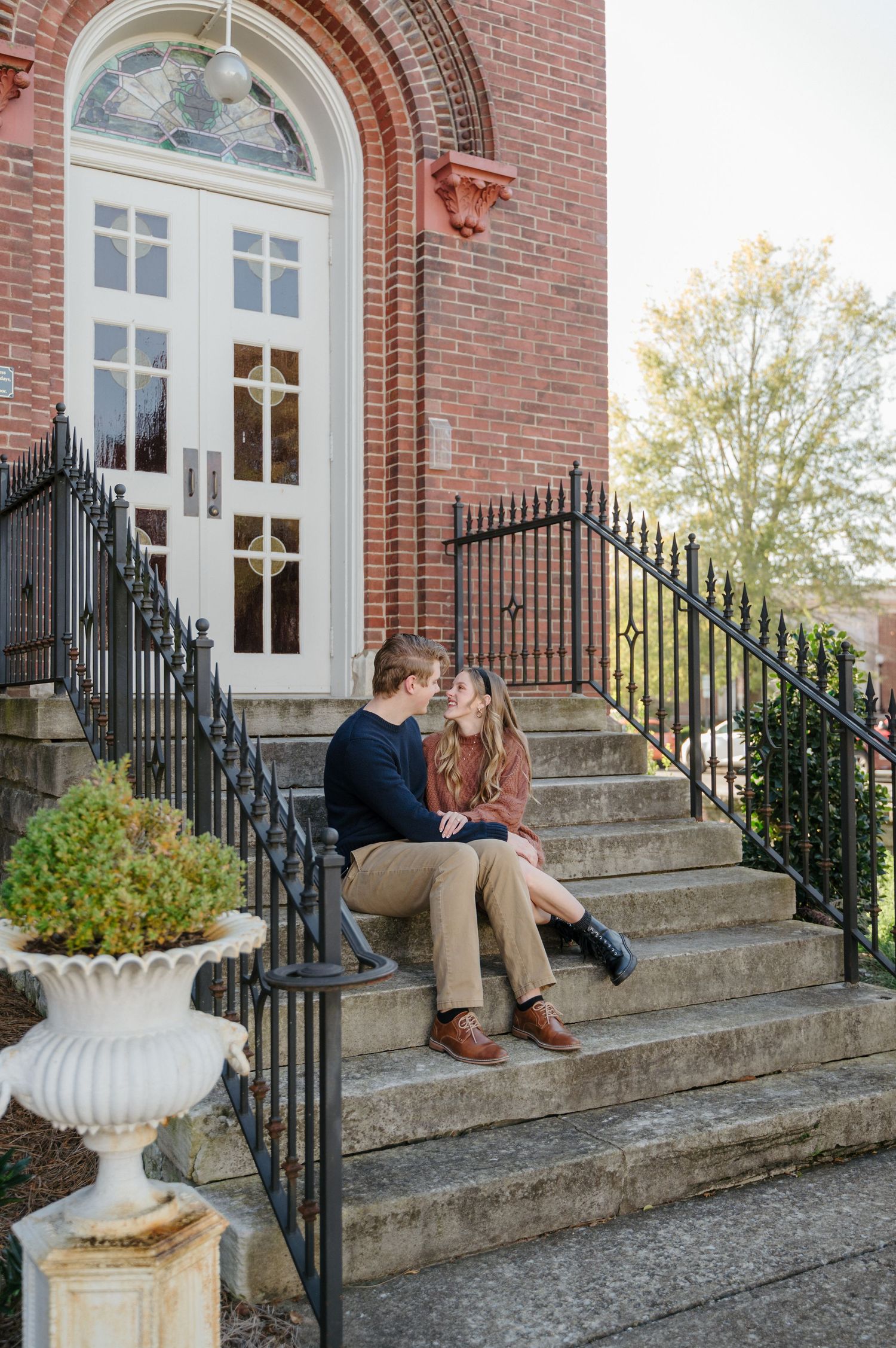 A couple sits on the steps of an old chapel on a crisp fall day