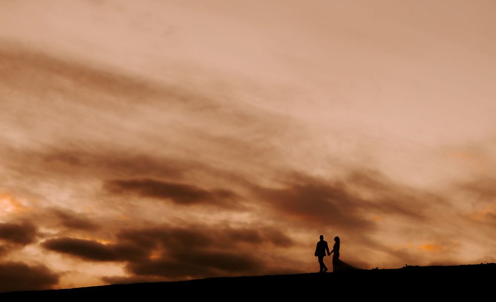Silhouettes of two people walking together against a dramatic orange and brown sunset sky.
