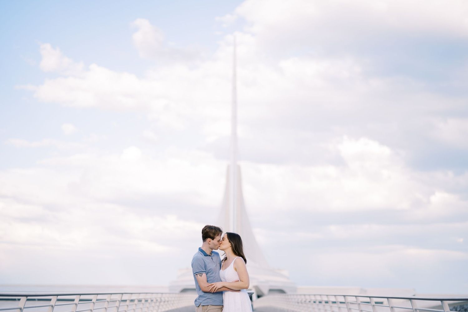 A romantic couple embrace in front of the iconic Eiffel Tower in Paris on a bright cloudy day.