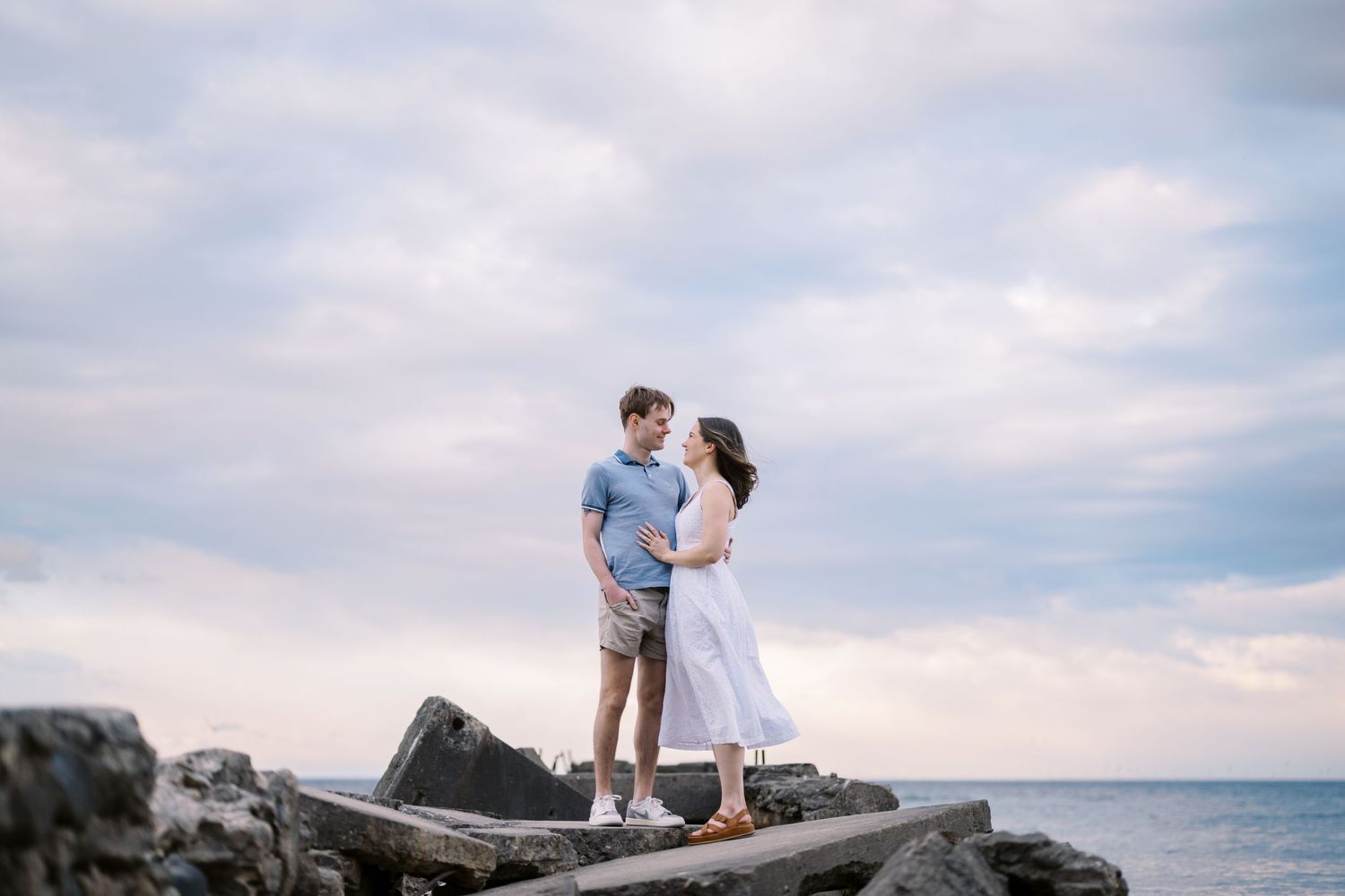 Couple shares an intimate moment while standing on rocky coastal outcropping by the ocean.