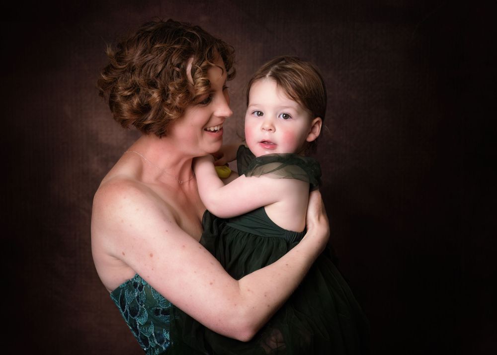 A warm studio portrait against a dark brown background, showing an intimate embrace captured in soft lighting.