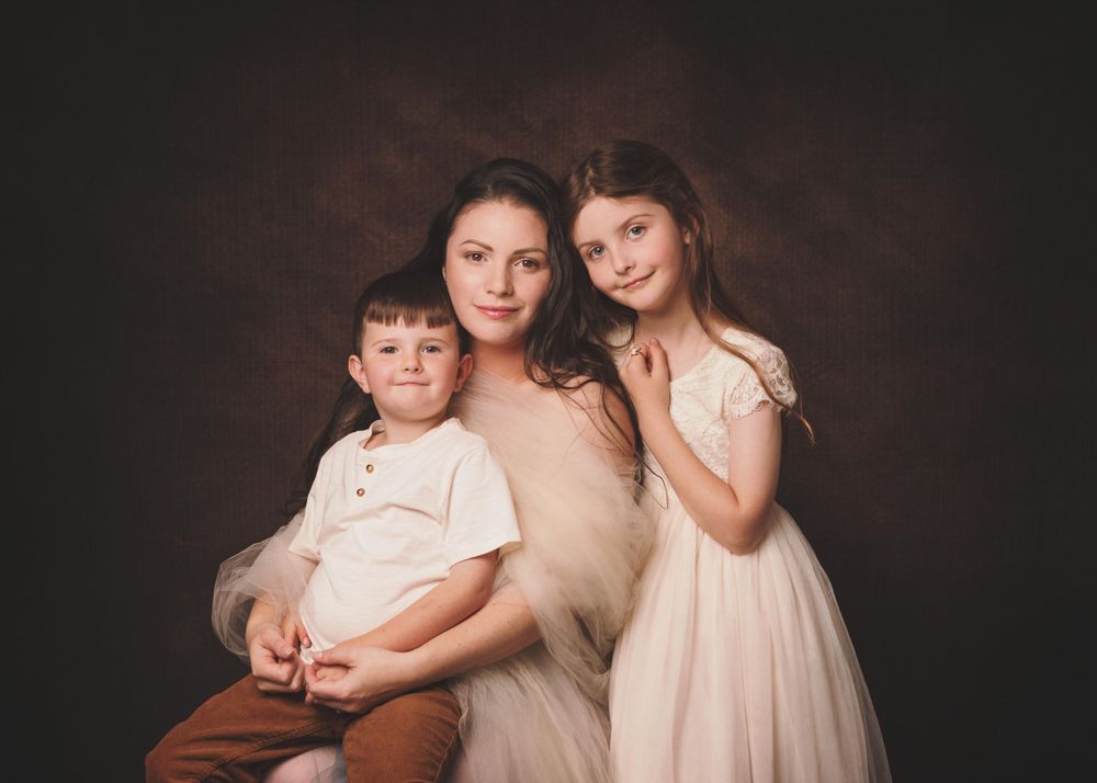 Elegant studio portrait of a family in soft neutral tones against a dark background.