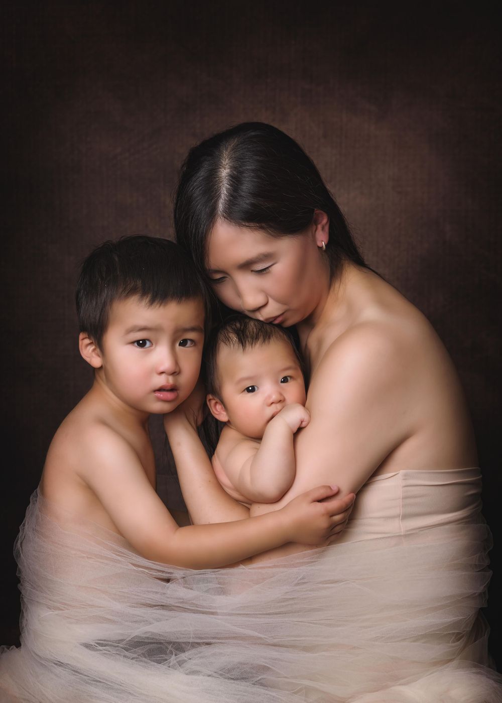 Artistic family portrait in soft beige tones showing tender embrace against dark brown background.