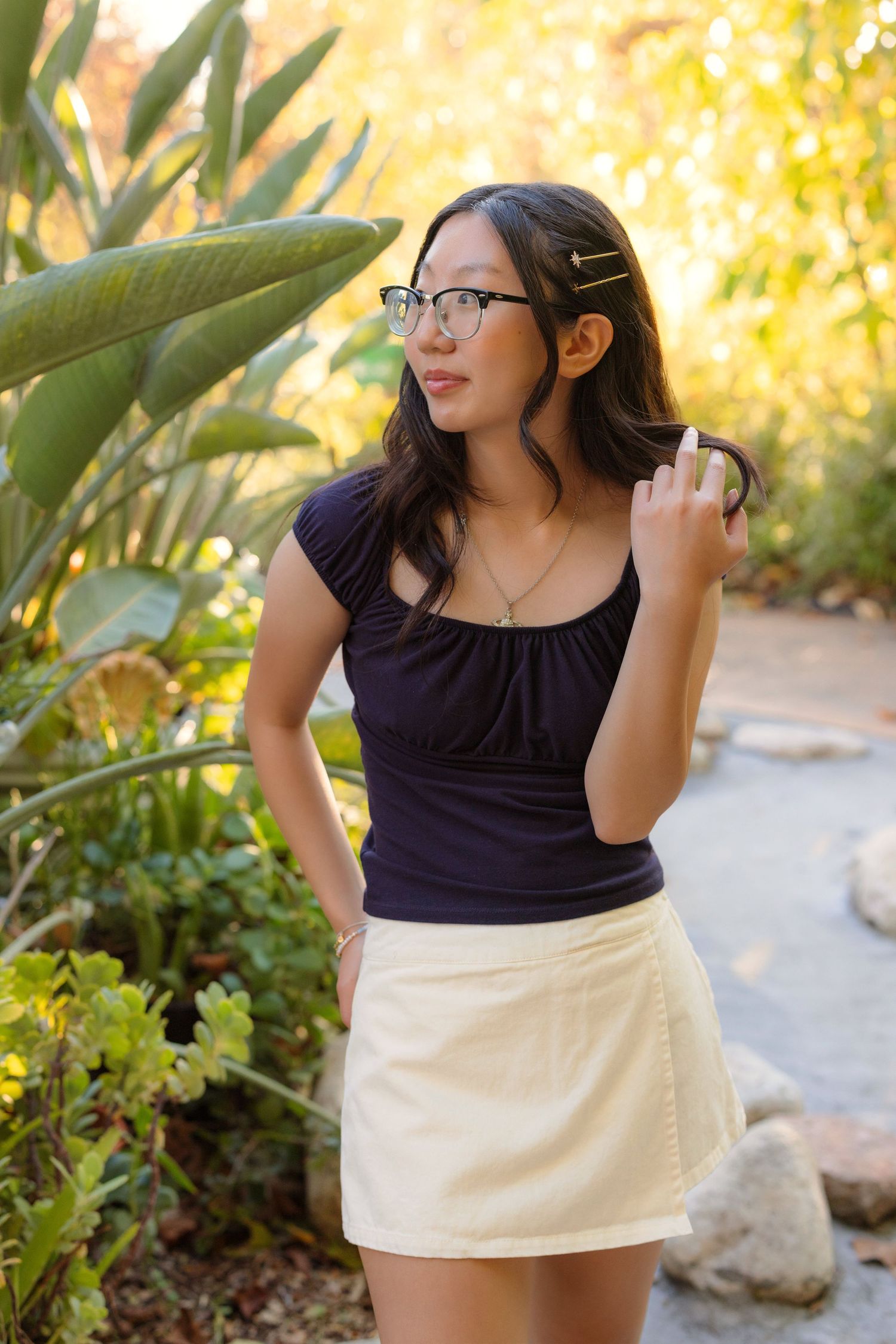 Person in black top and white skirt standing by tropical plants in garden.