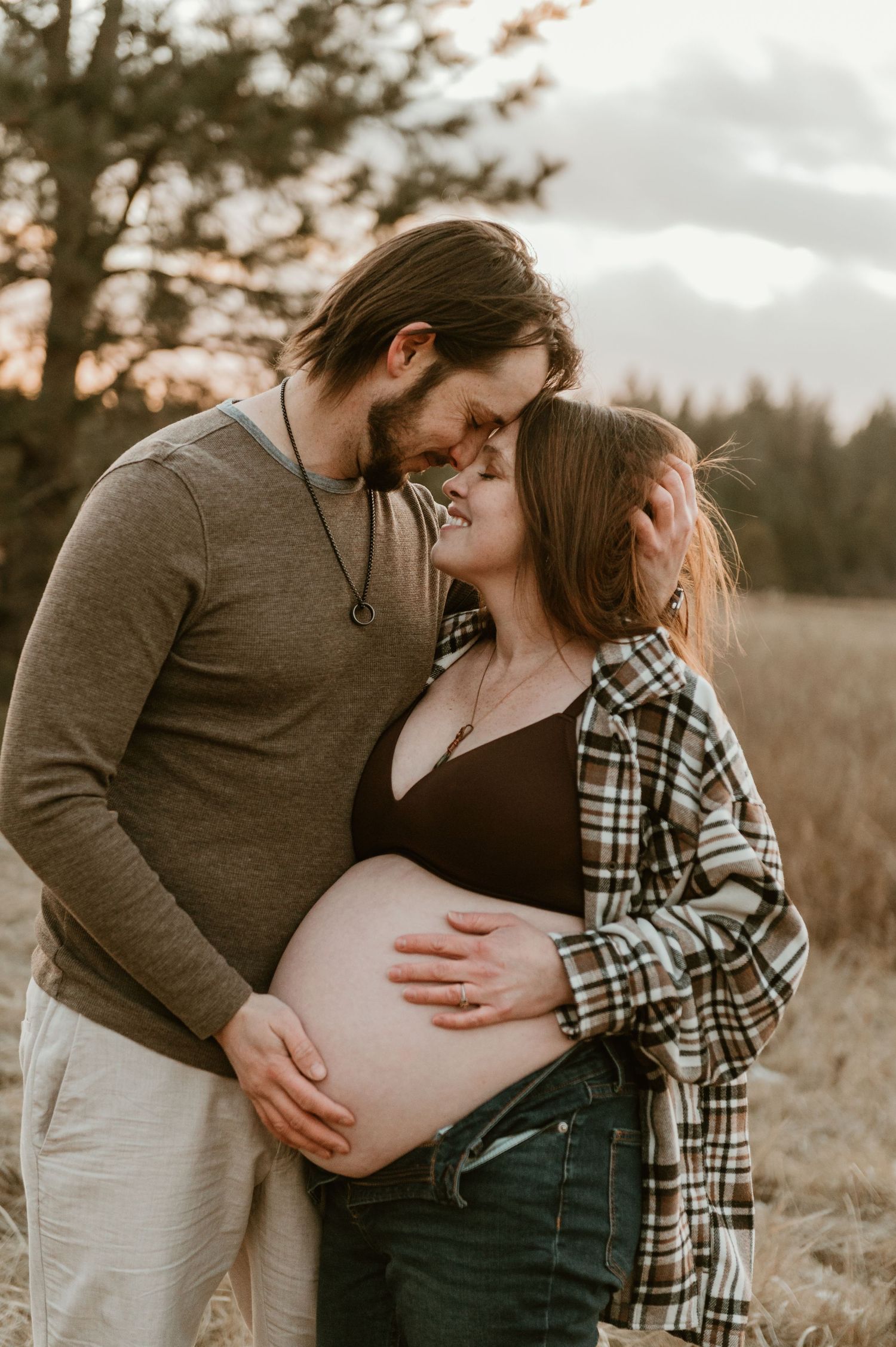 An intimate maternity photo of a couple embracing at sunset in a rural field.