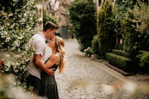 Romantic couple embraces on a charming cobblestone path surrounded by lush greenery on a sunny afternoon.