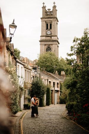 A cobblestone street in Edinburgh curves past historic buildings with a tall church clock tower rising in the distance.