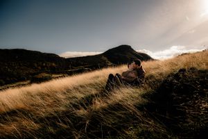 Golden sunlit grass sways on a mountainside against a moody sky during sunset.