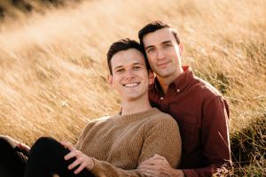 Two people embracing in a wheat field during golden hour with soft sunlight illuminating the scene.