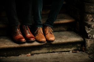 Two pairs of brown leather classic Oxford dress shoes on worn stone steps in moody lighting.