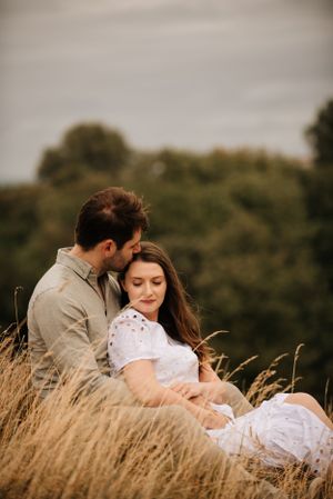 A tender moment between a couple sitting in tall golden grass during sunset.