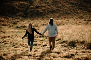 A couple holding hands while walking up a golden sunlit hillside during sunset.