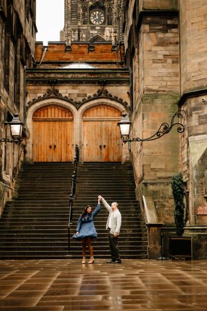 Two people stand on stone steps leading to grand wooden double doors of a historic Gothic church building in Edinburgh.