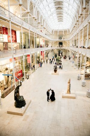 Interior view of a historic Victorian shopping arcade with glass ceiling and statues displaying retail stores on multiple levels.