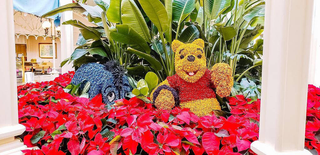 Colorful display of red poinsettias and Winnie the Pooh characters surrounded by white pillars and tropical plants.