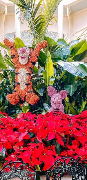 A vibrant display of orange and pink plush toy decorations among tropical plants and bright red poinsettias.