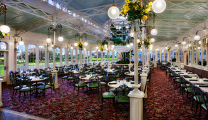 Elegant dining room interior with glowing globe lights, burgundy carpeting, and multiple seating areas stretches into panoramic view.