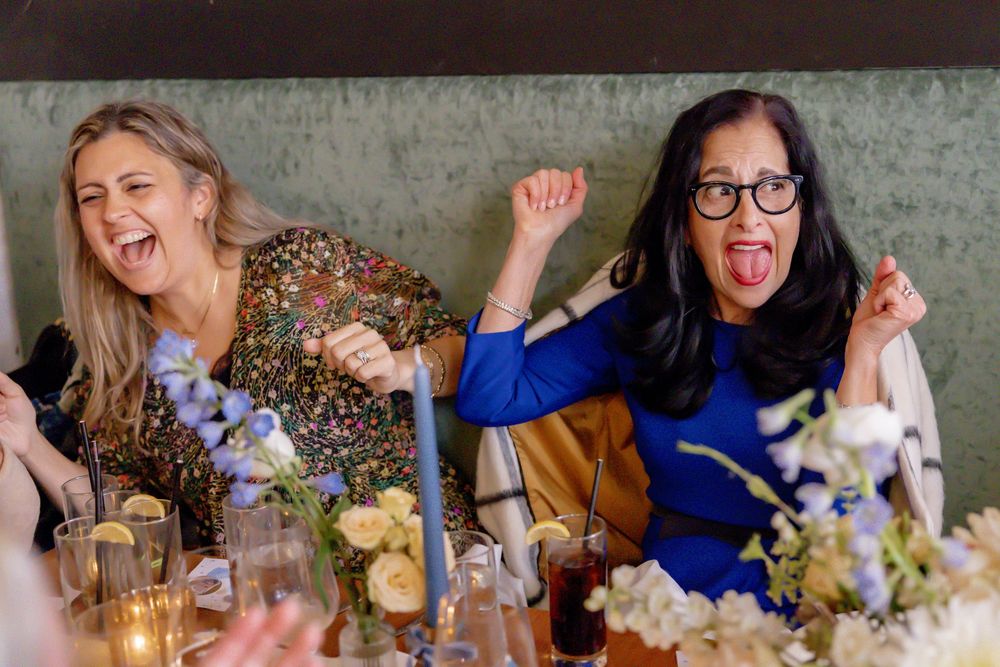 Two women making funny faces and gesturing at a floral decorated celebration dinner table.