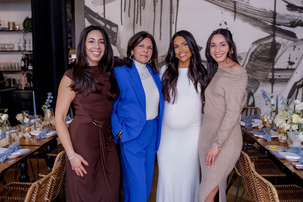 Four elegantly dressed women smiling together at an upscale restaurant event.