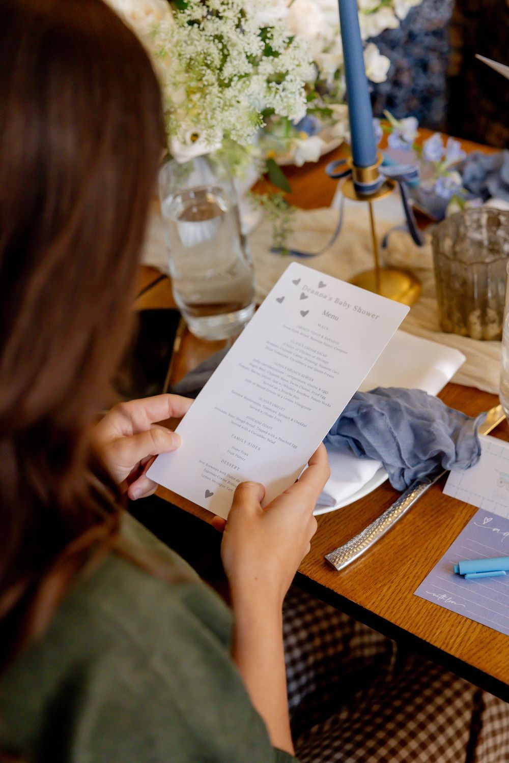 Woman reading a wedding menu card at an elegantly decorated table with blue candles and floral arrangements.