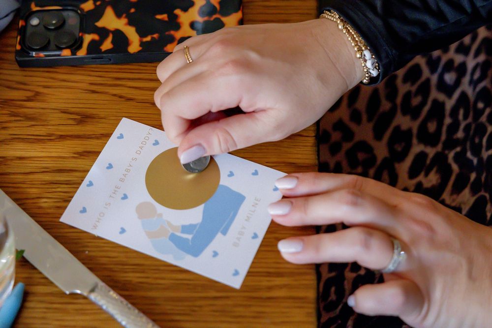 Woman scratching a gold foil scratch-off card with blue heart designs on a wooden table.