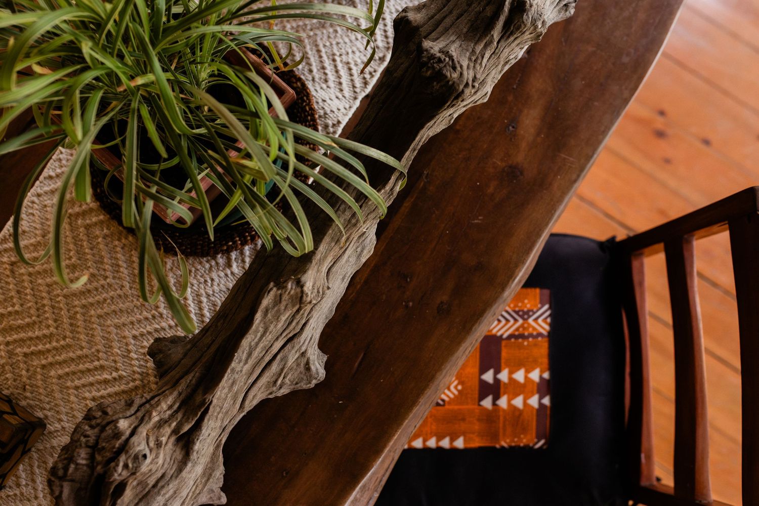 Rustic driftwood console table with a spider plant and woven basket on hardwood floors near a black chair.