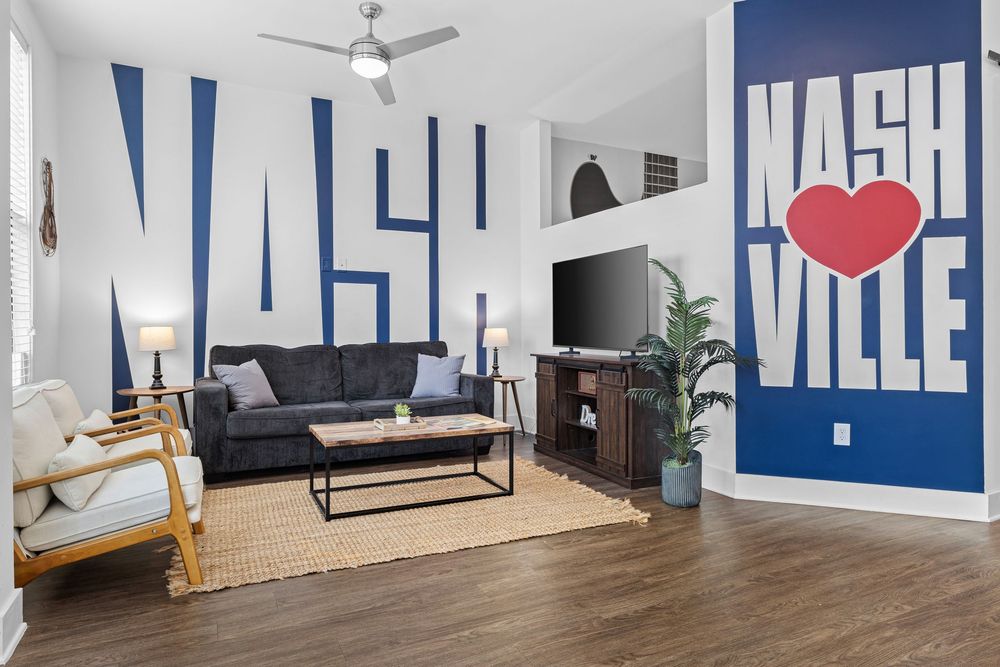 Nashville-themed living room with bold blue wall murals, dark sofa, hardwood floors, and ceiling fan.