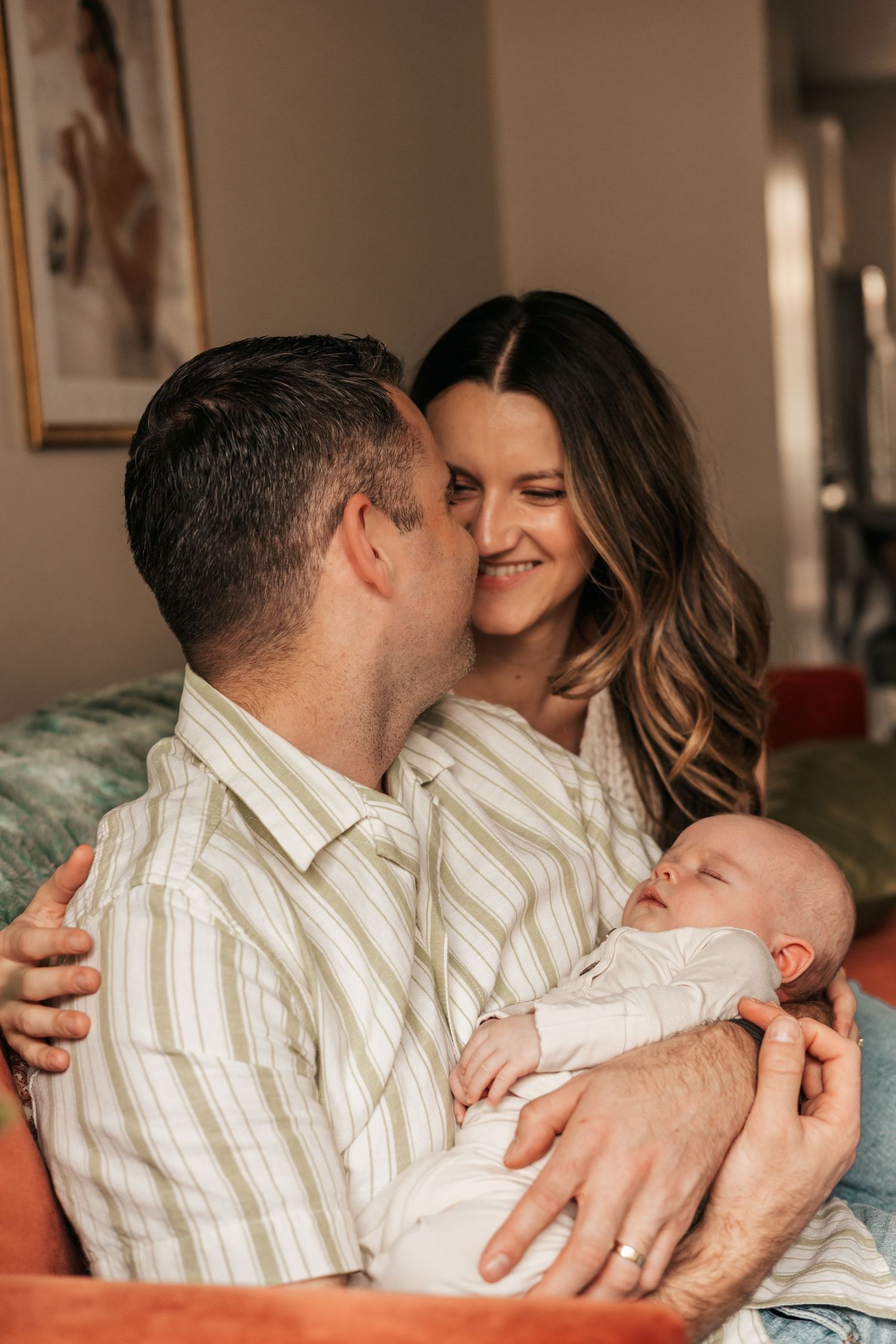 A happy couple smiles while cradling their newborn baby indoors | Newborn Photographer in Broomfield Colorado