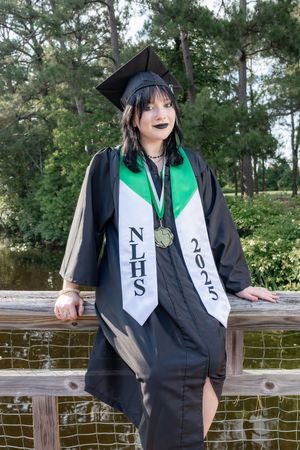 A high school graduate poses in black cap and gown with NLHS 2025 stole and medal outdoors.