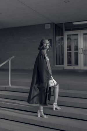 Black and white photo of a smiling graduate in cap and gown on school steps.