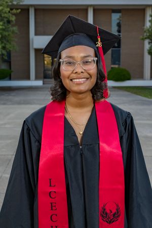 Smiling graduate in black cap and gown with red LCEC stole poses outdoors.
