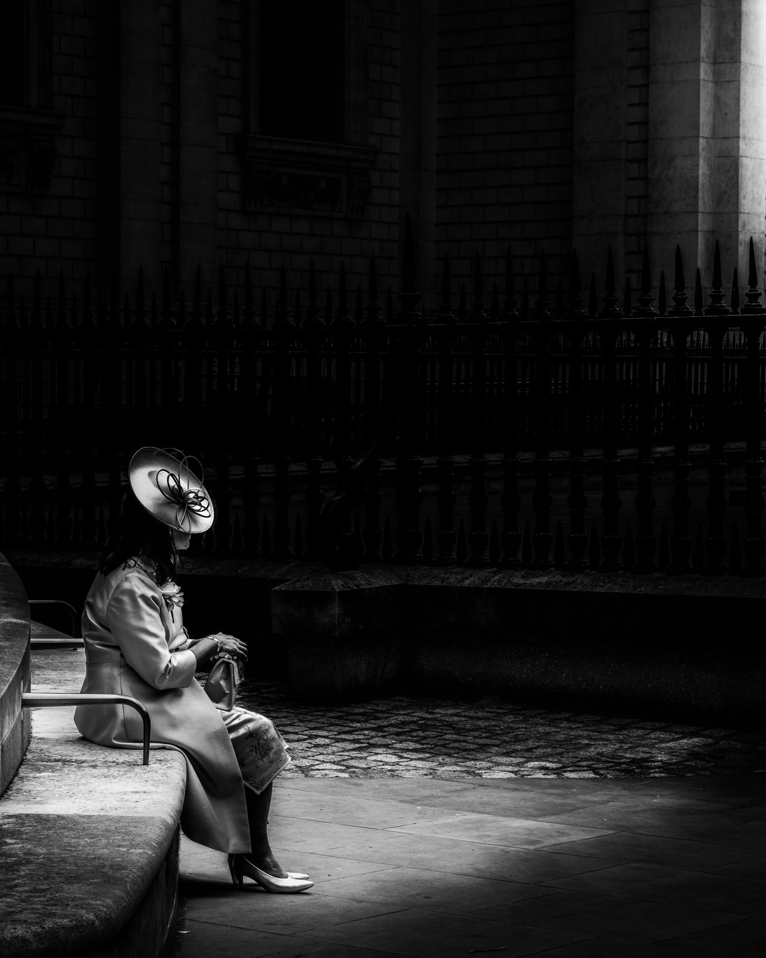 Black and white photo of a person sitting on a bench in dramatic light and shadow