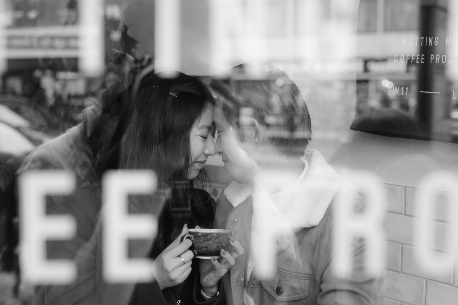 Two women enjoying coffee at Notting Hill Coffee Project cafe window with iconic red double-decker bus in background.