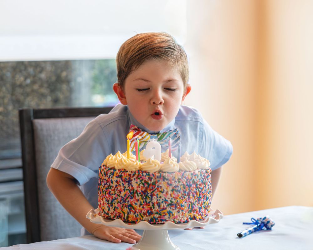 Colorful sprinkled birthday cake with lit candles being blown out at a table with festive decorations.