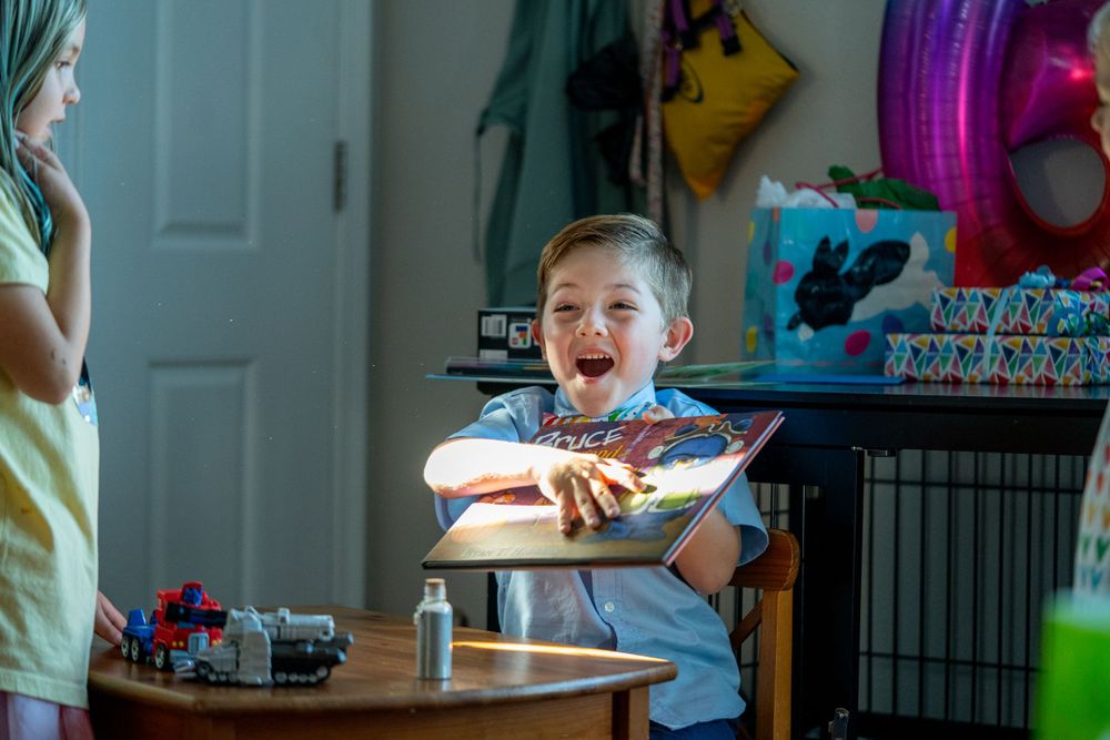 Young child sitting at a table with lit birthday candles glowing in a dimly lit room during a celebration.