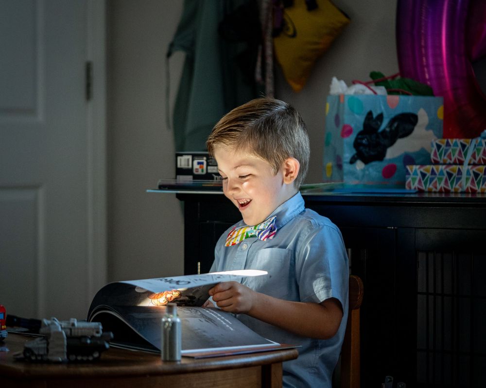 Young student does homework at desk illuminated by bright lamp light in dark room.