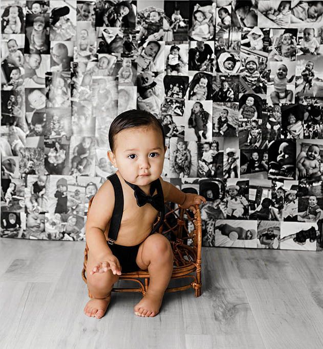 A baby boy in suspenders sits in a wicker chair against a black and white photo collage backdrop.