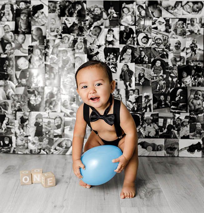 Baby boy in bow tie holds blue balloon near ONE blocks, celebrating first birthday with black and white photo collage backdrop.