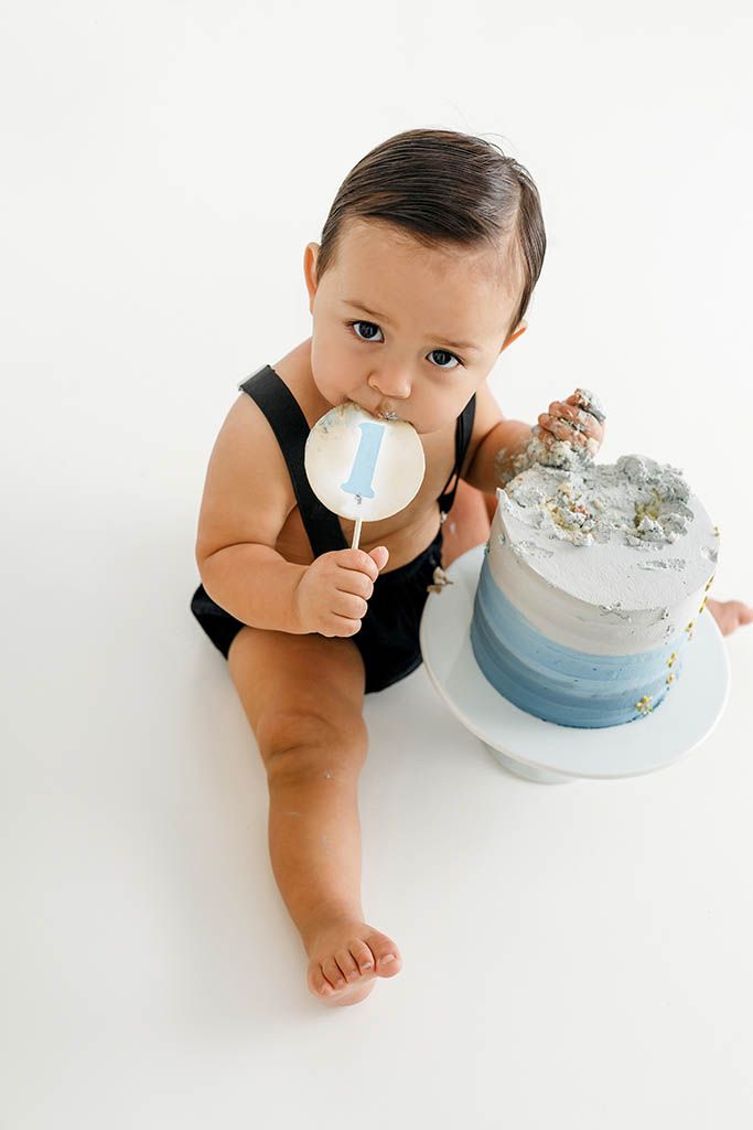 Baby boy in black romper smashing his first birthday cake while holding a number one by Winchester cake smash photographer.
