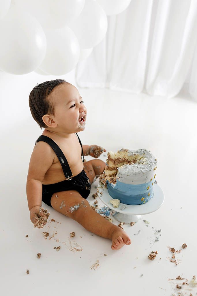 Happy baby enjoying messy cake smash at 1st birthday session in Winchester California photography studio.